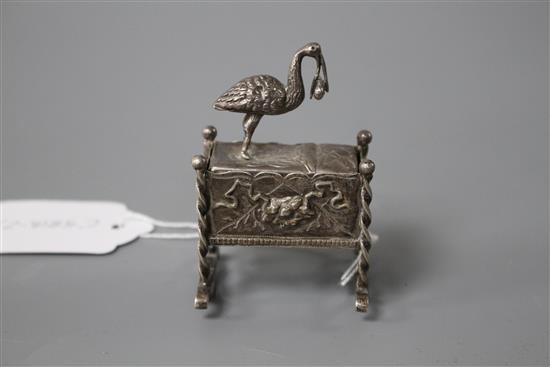 An early 20th century continental white metal novelty box and cover, modelled as a stork with baby upon a cradle,